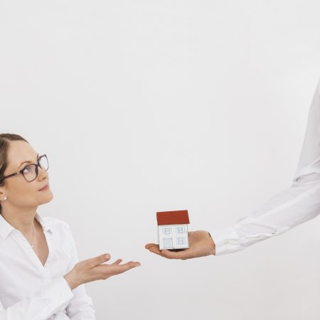 man s hand giving miniature house model young woman against white wall